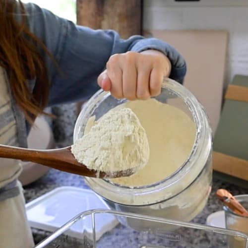 adding-einkorn-flour-into-the-bucket-of-water-yeast-and-reserveddough
