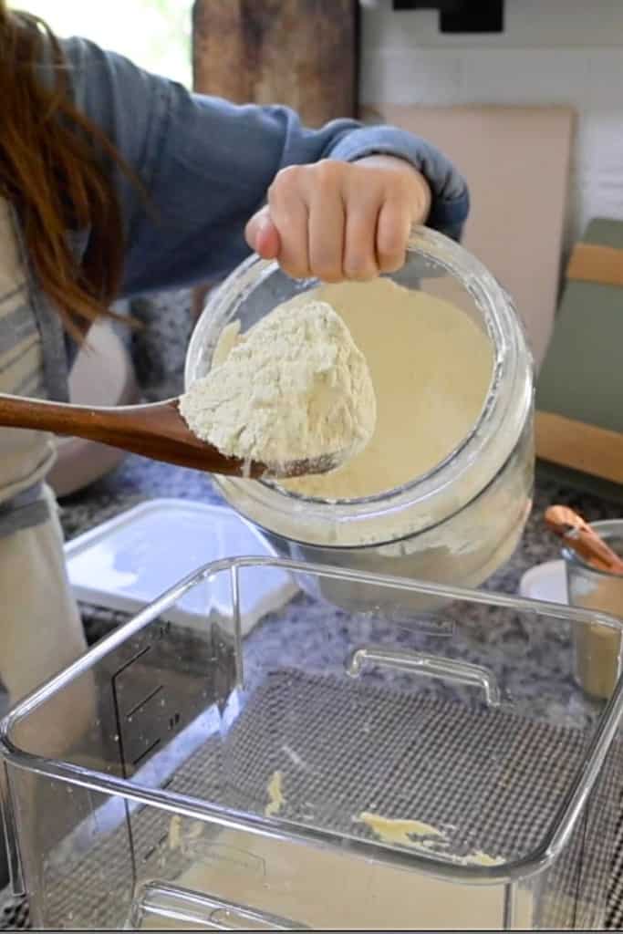 adding-einkorn-flour-into-the-bucket-of-water-yeast-and-reserveddough